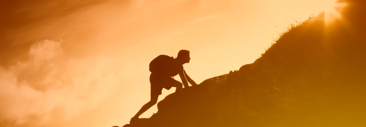 Silhouette of man climbing up a mountain