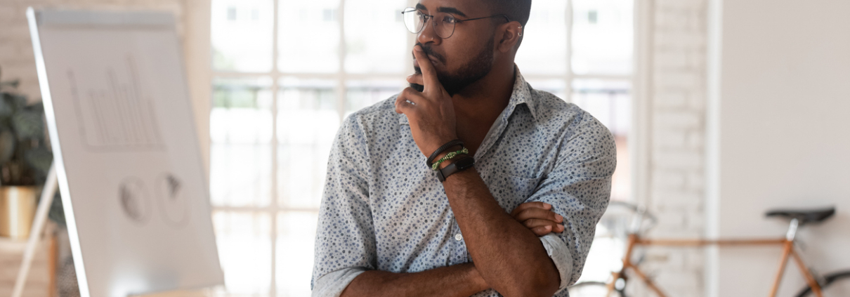 Pensive concerned african employee touch chin looking away leaned on table thinking inside of modern office boardroom, company owner boss search solution solve business issues or make decision concept