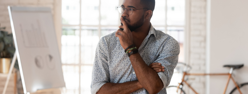 Pensive concerned african employee touch chin looking away leaned on table thinking inside of modern office boardroom, company owner boss search solution solve business issues or make decision concept